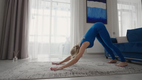 Young-Woman-Meditating-Sitting-on-Carpet-and-Doing-Splits-stretching-Doing-Yoga-Blue-Sportswear-Light-Room-At-Home-In-the-Morning.-woman-practicing-yoga-at-home